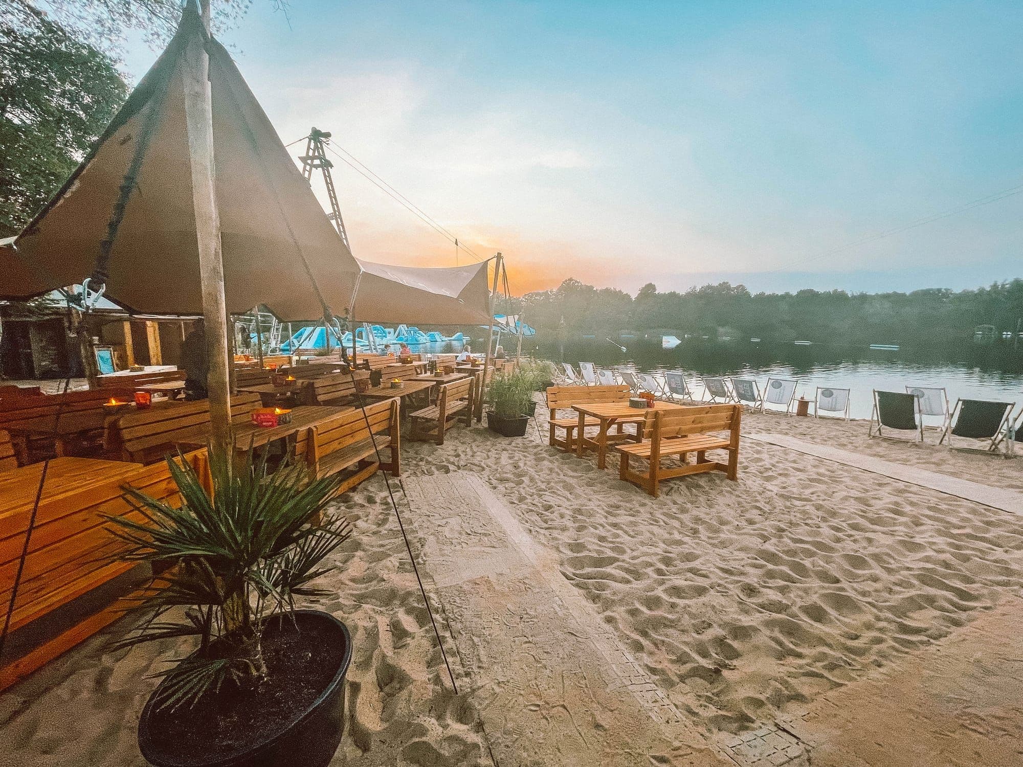 Beachclub am Oyter See bei Sonnenuntergang mit Sonnensegeln, Holzbänken und Liegestühlen im Sand